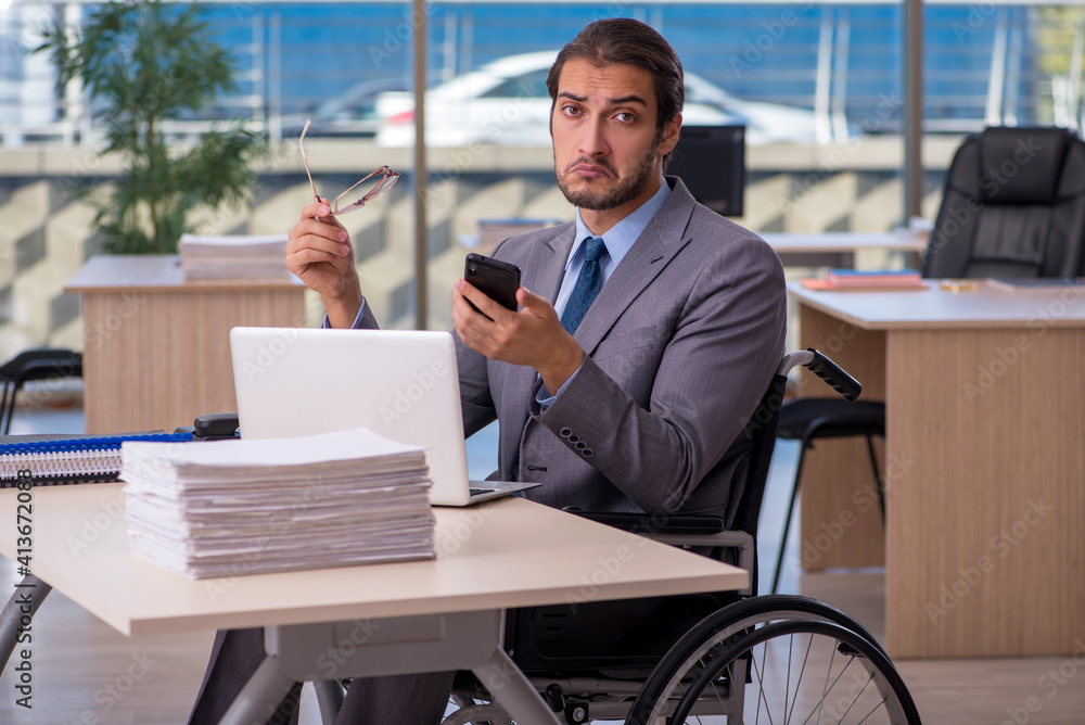 Young male employee in wheel-chair working in the office Young male employee in wheel-chair working in the office