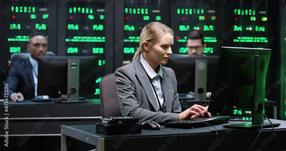 Smart female IT worker sitting in server room behind workplace, working with database on computer. System software concept. Smart female IT worker sitting in server room behind workplace, working with database on computer. System software concept.