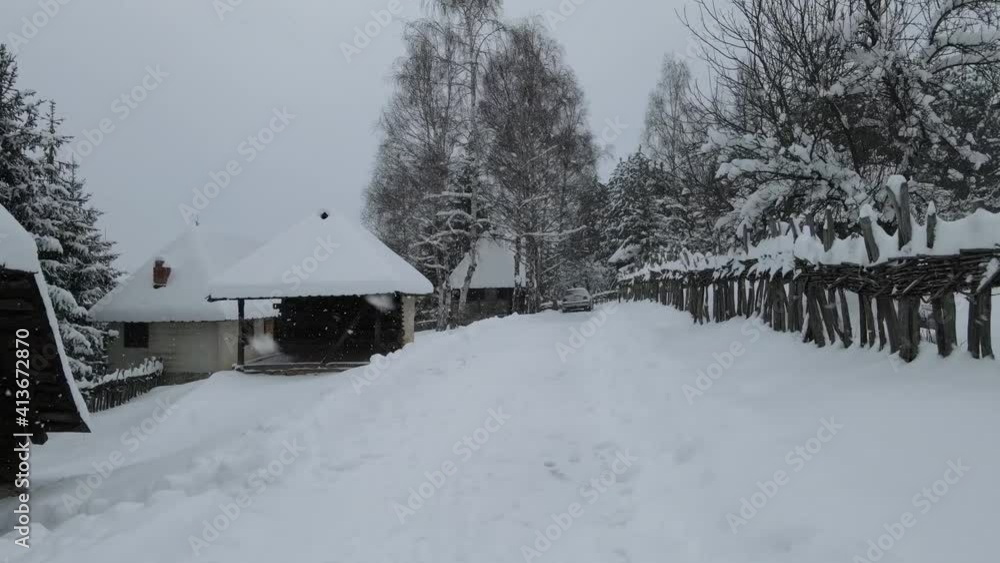 Low flying drone shot through snow falling with wooden fence and cabins and trees covered with snow. Low flying drone shot through snow falling with wooden fence and cabins and trees covered with snow.