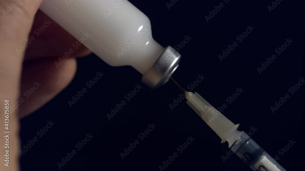 A syringe needle penetrates a vial of milky medication in preparation to give an injection to a patient - isolated black background A syringe needle penetrates a vial of milky medication in preparation to give an injection to a patient - isolated black background