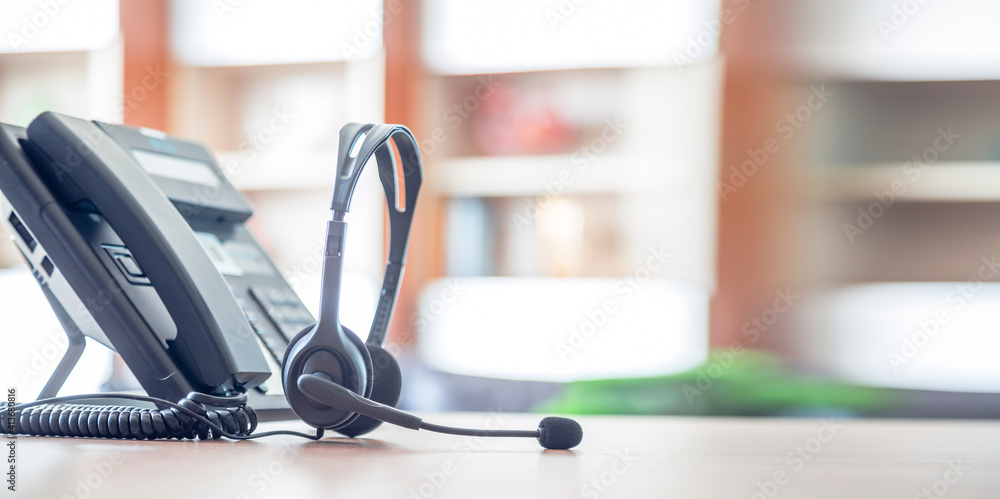 Close up soft focus on headset with telephone devices at office desk for customer service support.VOIP headset for customer service support (call center) concept. Close up soft focus on headset with telephone devices at office desk for customer service support.VOIP headset for customer service support (call center) concept.