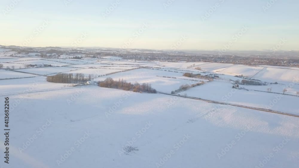 Undisturbed winter landscape with a house and fields covered with white snow till the horizon on a bright cold day in Scotland during golden hour. Drone dolly shot Undisturbed winter landscape with a house and fields covered with white snow till the horizon on a bright cold day in Scotland during golden hour. Drone dolly shot