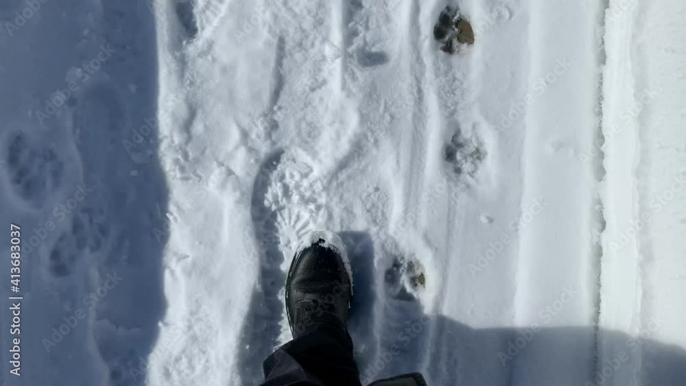 Person with black boots walking on a snow covered sidewalk on a sunny day. Person with black boots walking on a snow covered sidewalk on a sunny day.