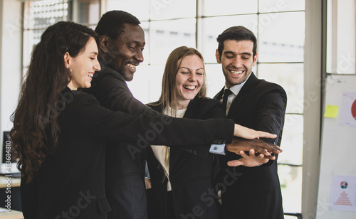 Group of four happy multiracial businesswomen and businessmen putting their hands together to celebrate their successful project with smiling. Teamwork concept of a new start-up business company