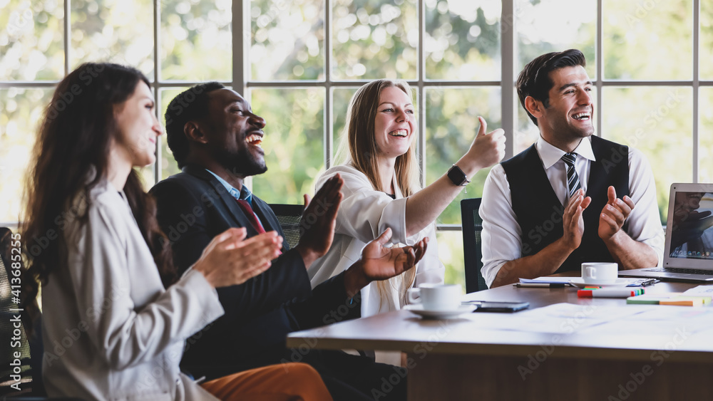 Group of four professional multiethnic businessmen and businesswomen sitting, clapping hands and showing thump up gesture to celebrate the new project in a company meeting at office working table Group of four professional multiethnic businessmen and businesswomen sitting, clapping hands and showing thump up gesture to celebrate the new project in a company meeting at office working table