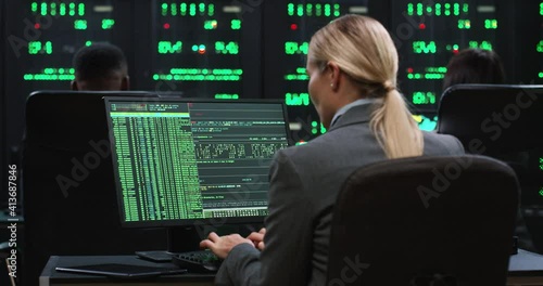 Blonde female programmer sits at computer in server room and works with database. System software concept. View from back. photo