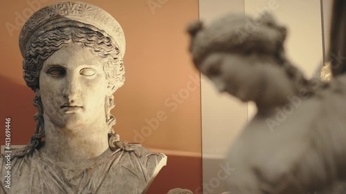 Ancient antique statue of a young woman in a museum with moody warm lights and a head of a bigger woman statue in the background. Smooth dolly sliding movement with parallax effect in 4K. photo