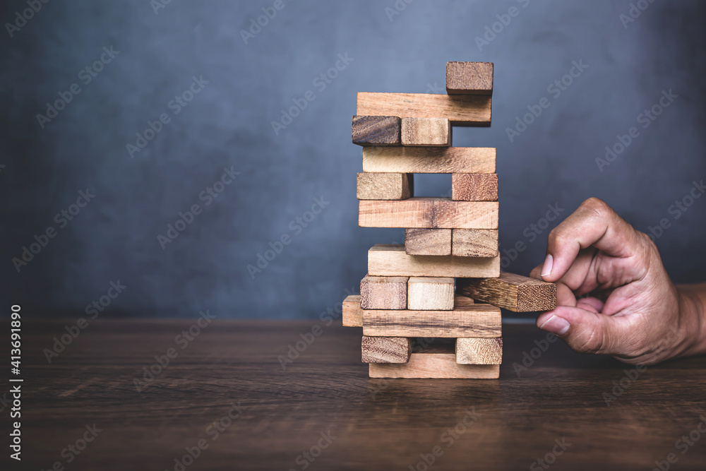 Close-up hand pull wooden block from other the wood block stacked in tower shape concepts of financial risk management and strategic planning. Close-up hand pull wooden block from other the wood block stacked in tower shape concepts of financial risk management and strategic planning.