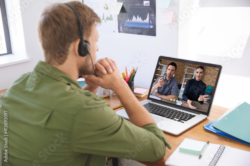 Caucasian man in office having video call with two colleagues displayed on laptop screen