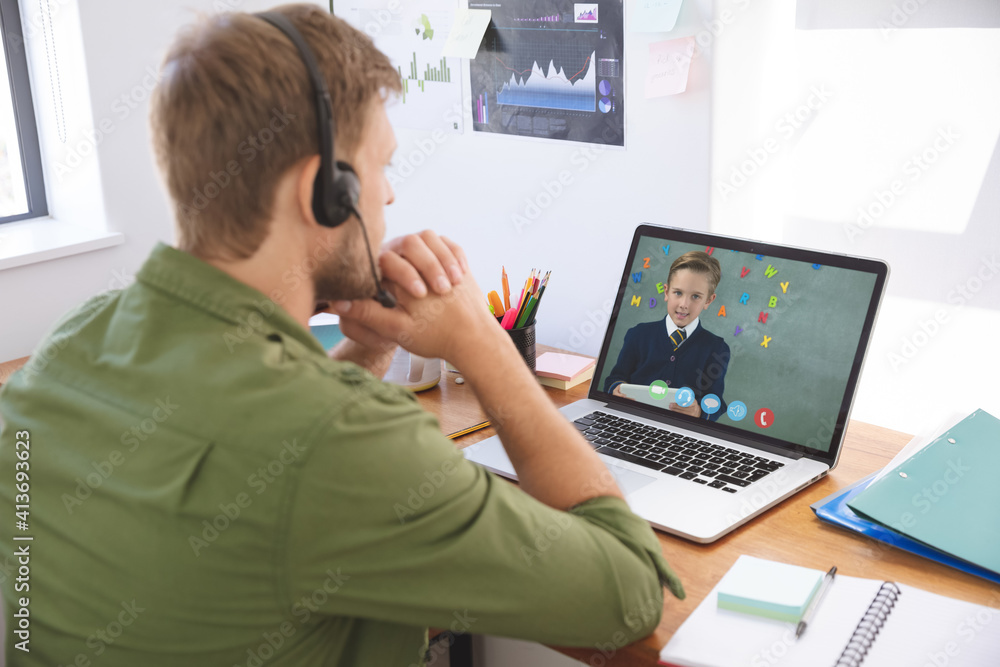 Caucasian male teacher using laptop and phone headset on video call ...