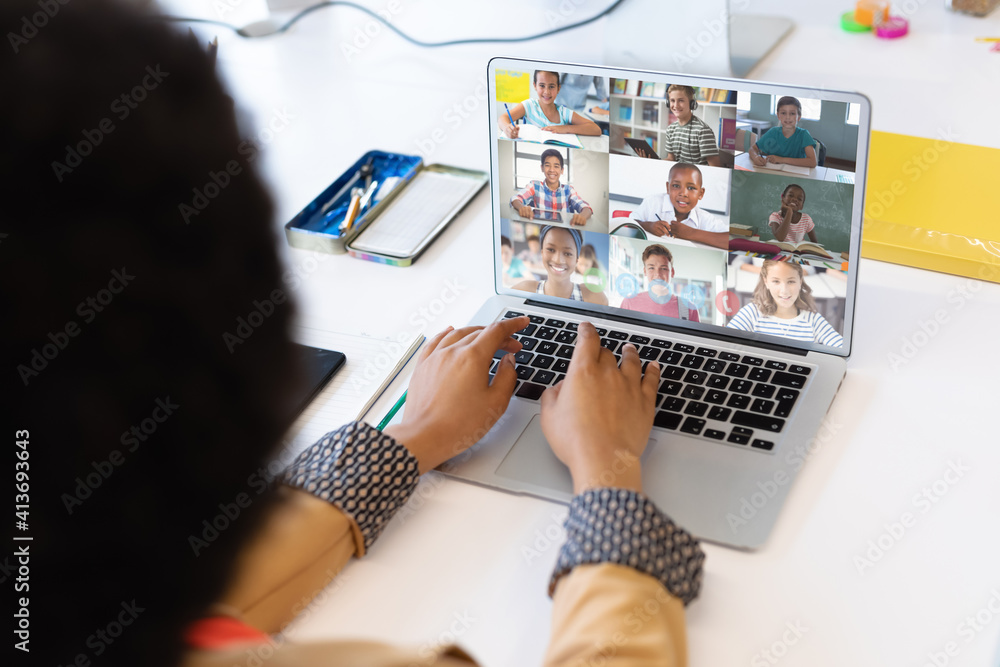 Mixed race female teacher using laptop on video call with school ...