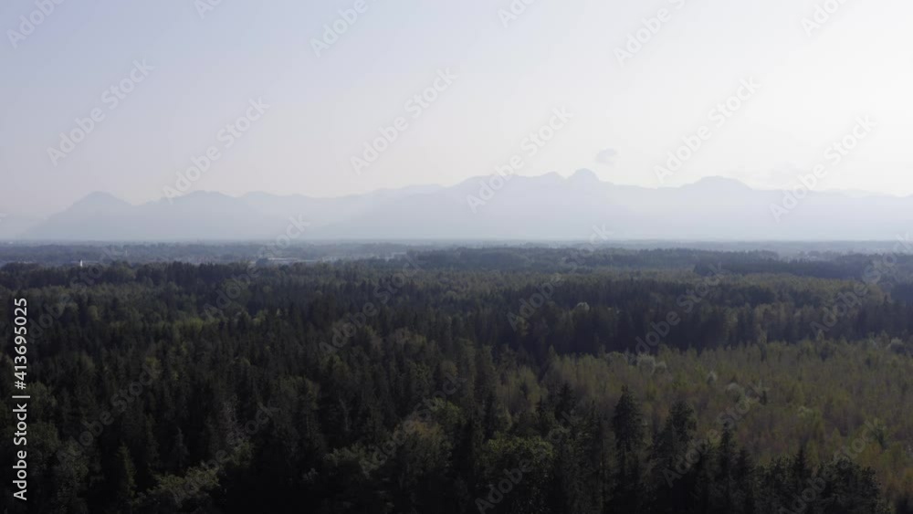 Aerial view of dense forest with hazy mountains in the background. Slow push in on the Bavarian Alps. Aerial view of dense forest with hazy mountains in the background. Slow push in on the Bavarian Alps.