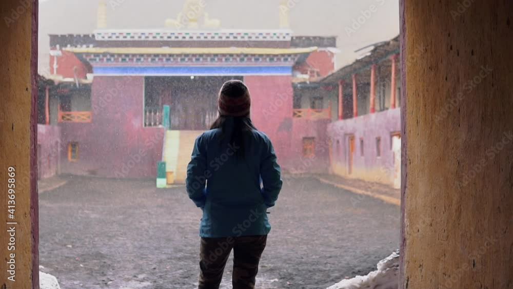 A Female Backpacker Standing During Snowfall, Wearing a Jacket and Hat infront of a Monastery in Northern India in the Indo-Tibetan Border. A Female Backpacker Standing During Snowfall, Wearing a Jacket and Hat infront of a Monastery in Northern India in the Indo-Tibetan Border.