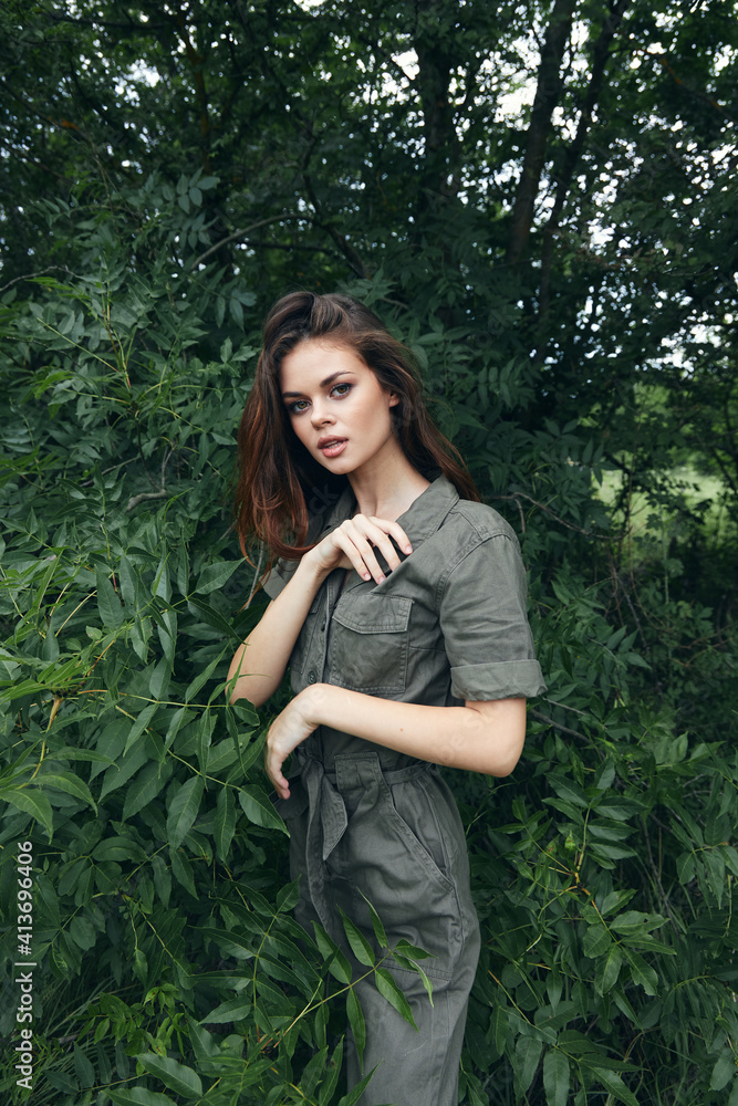 Woman in forest gestures with her hands and green jumpsuit fresh air