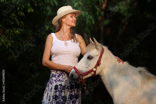 Girl in a cowboy hat with a white horse at sunset