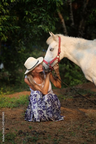 Girl in a cowboy hat with a white horse at sunset