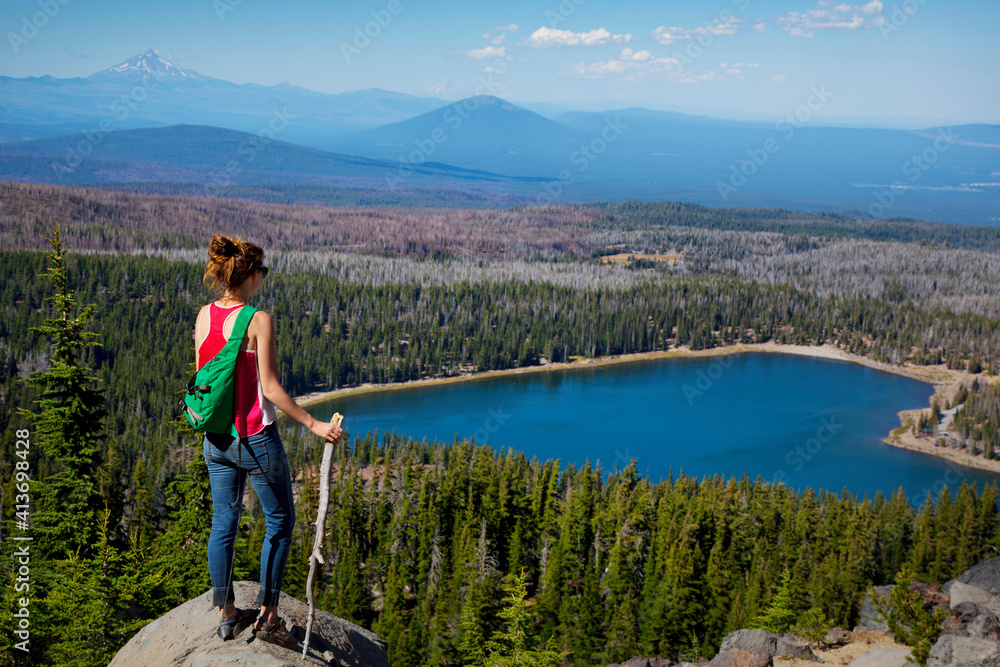 Female hiker looking at lake and trees while standing on top of cliff Female hiker looking at lake and trees while standing on top of cliff