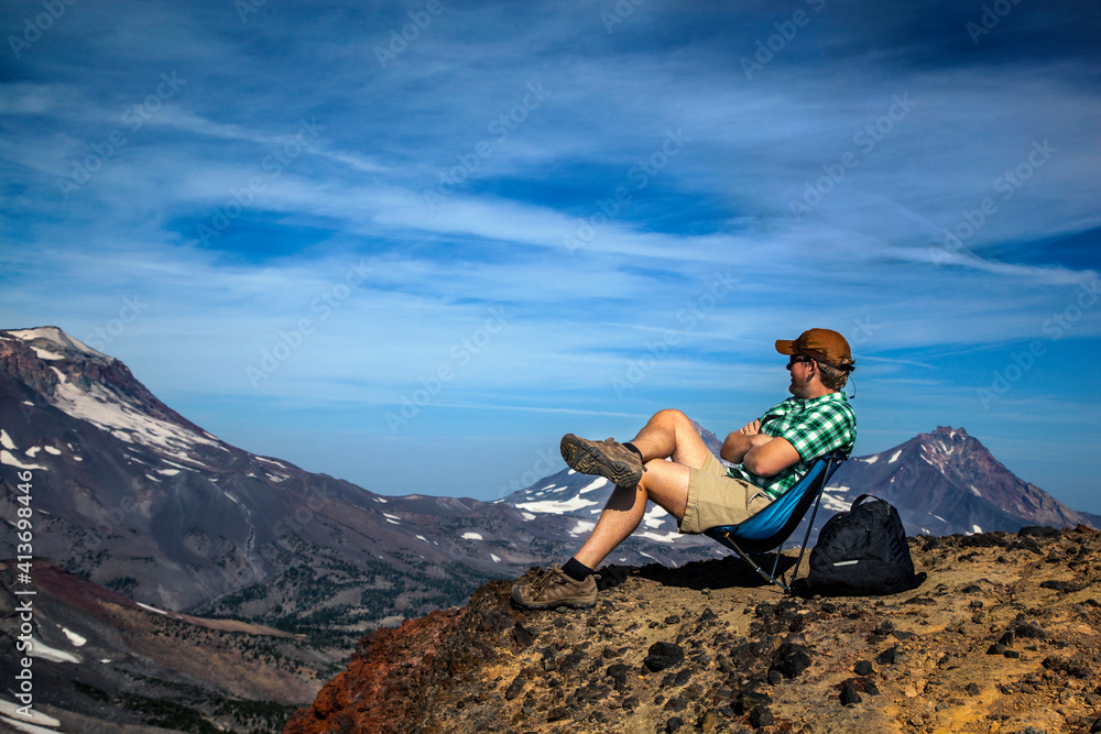 Hiker sitting on top of mountains against sky Hiker sitting on top of mountains against sky