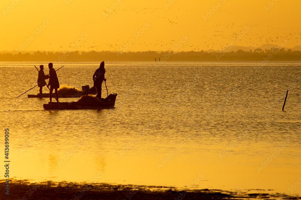 Silhouette view of the fishermen with their boats in a lake during sunset. Selective focus