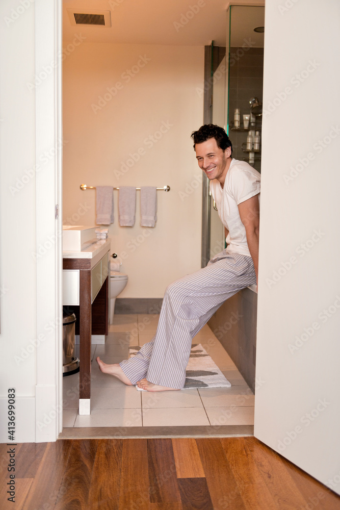 Cheerful man sitting on bathtub in bathroom Cheerful man sitting on bathtub in bathroom