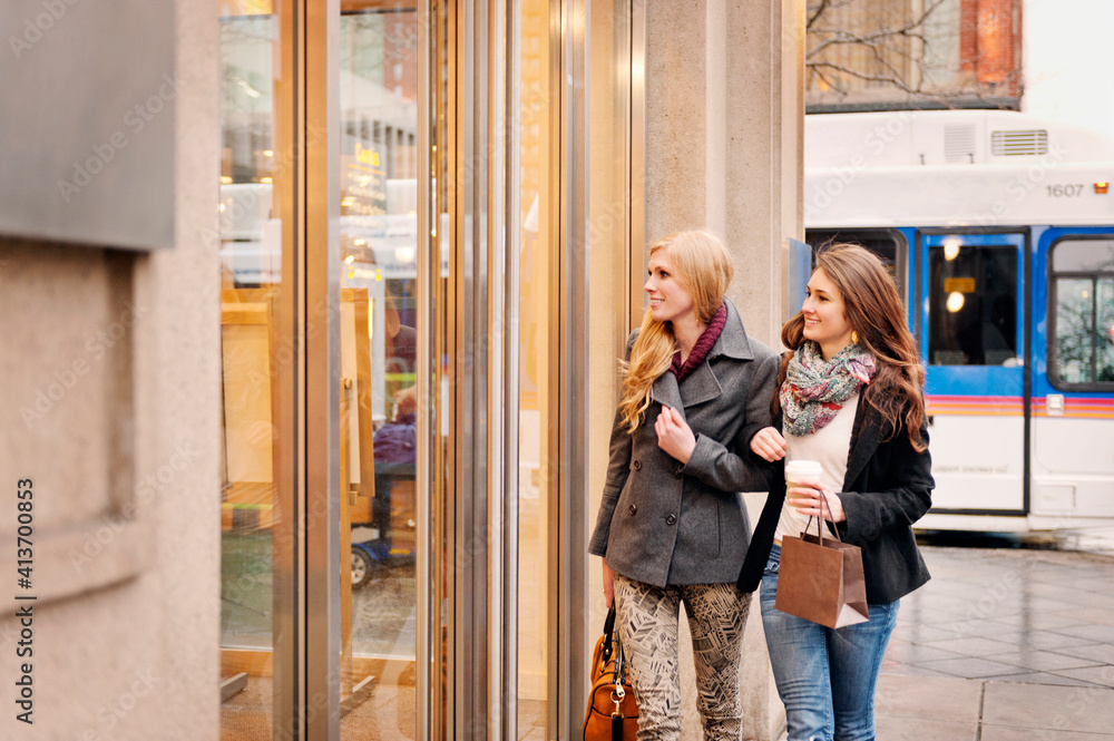 Smiling women looking at store while walking on sidewalk