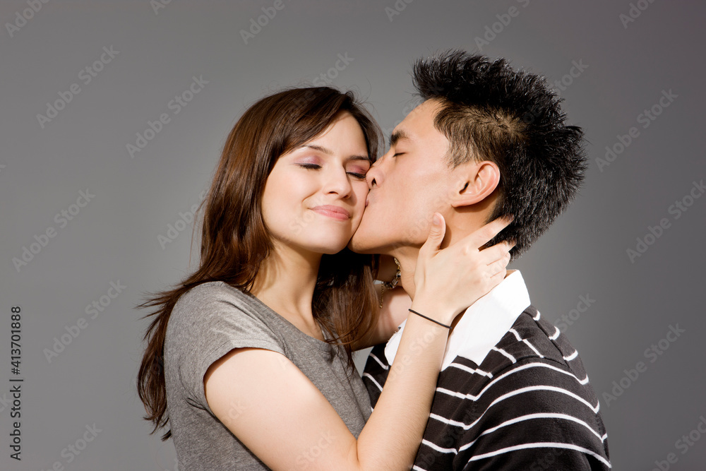 Man kissing woman against gray background Man kissing woman against gray background