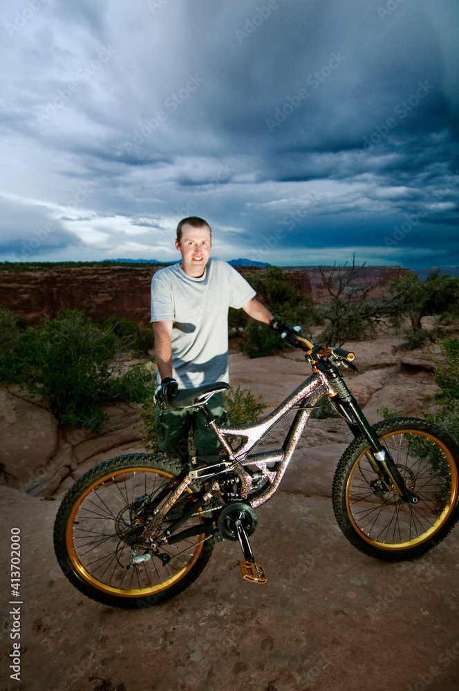 Portrait of man with bicycle standing on rocks against cloudy sky Portrait of man with bicycle standing on rocks against cloudy sky