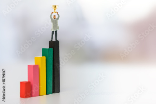 Self-made millionaire, become a long-term sustainable billionaire, a success leader and goal setting concept : Business tycoon raise a trophy cup or a globlet of winner on color wood pole bar graphs photo