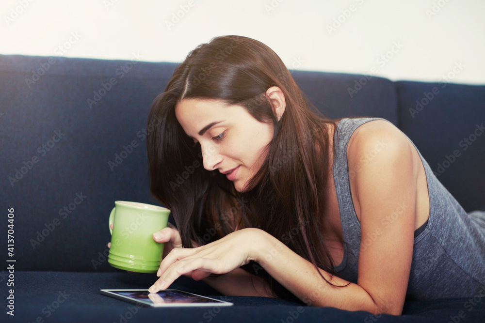 Beautiful woman using digital tablet while lying on sofa at home Beautiful woman using digital tablet while lying on sofa at home