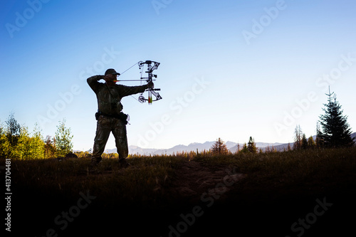 Hunter aiming with bow and arrow while standing against clear sky