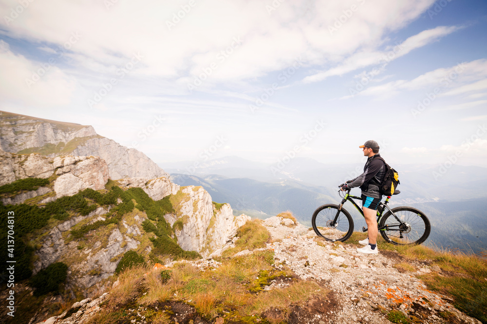Side view of man with bicycle standing on mountain against sky Side view of man with bicycle standing on mountain against sky