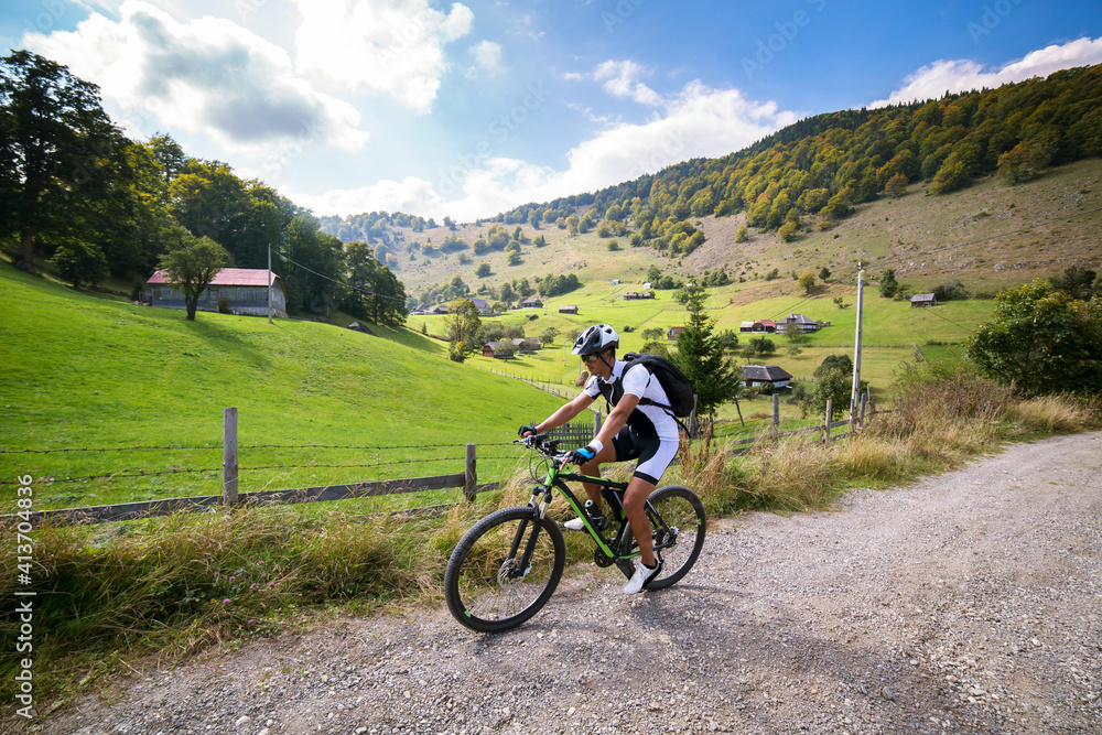 Male athlete cycling on dirt road by field against sky Male athlete cycling on dirt road by field against sky
