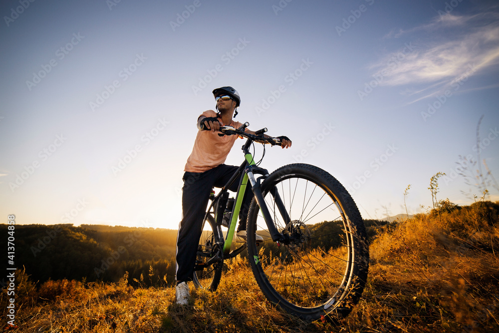 Male biker looking away while sitting on bicycle against sky Male biker looking away while sitting on bicycle against sky