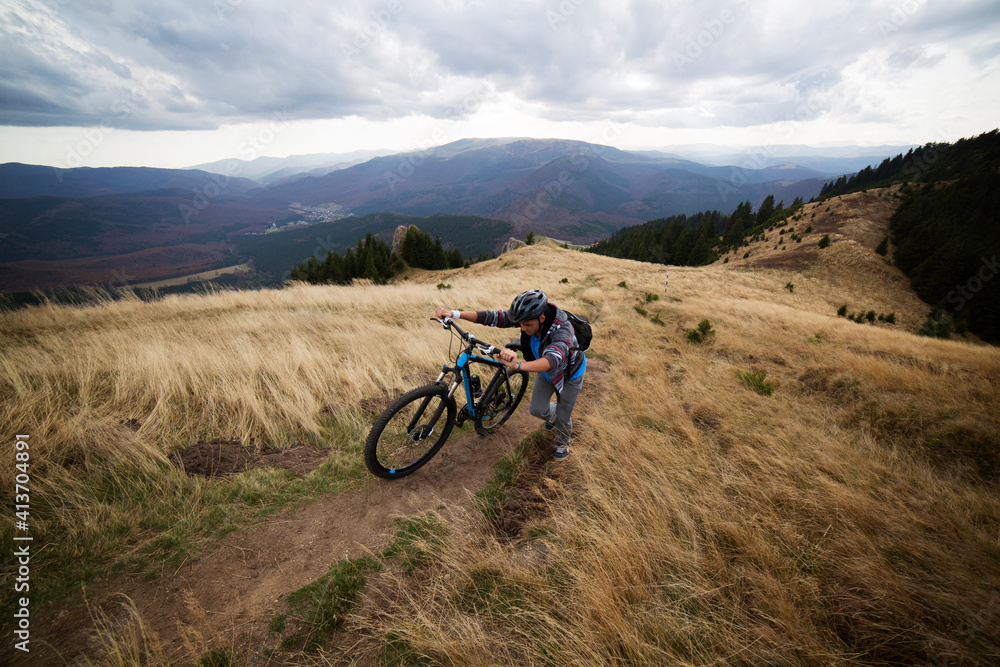 Male backpacker climbing with bicycle on mountain against cloudy sky Male backpacker climbing with bicycle on mountain against cloudy sky