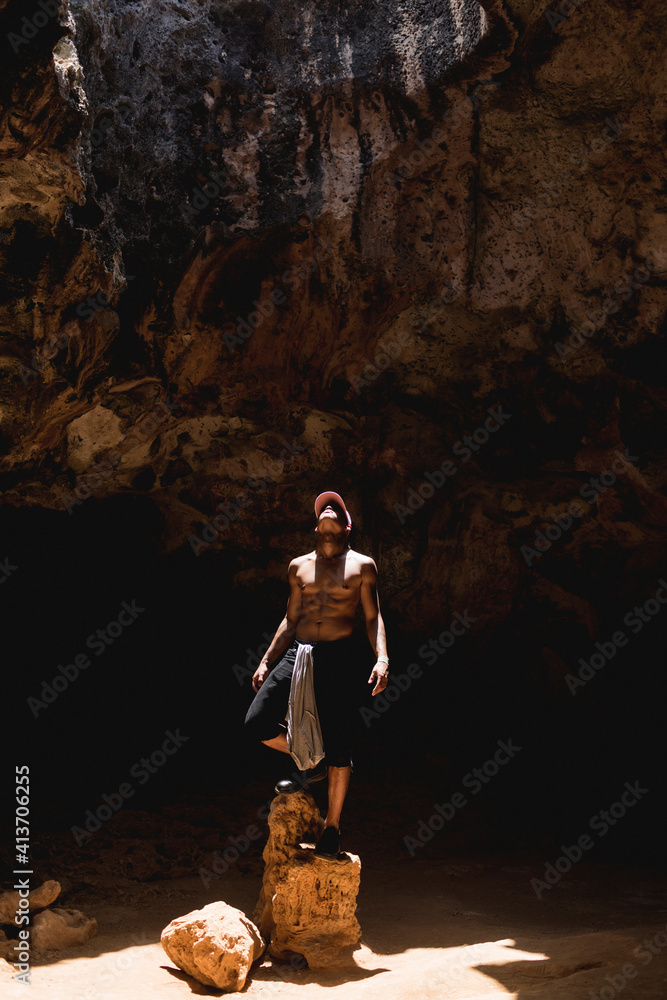 Man looking up while standing on rocks in cave Man looking up while standing on rocks in cave