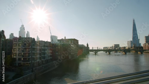 Beautiful cinematic pan of London City buildings and The Shard over the Thames River with sun star light rays, blue skies on a summer's day. photo