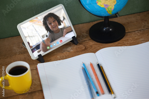 Mixed race schoolboy learning on tablet screen on desk during video call