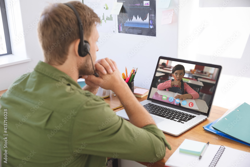 Male teacher wearing headphones having a video call with female student on laptop at home Male teacher wearing headphones having a video call with female student on laptop at home