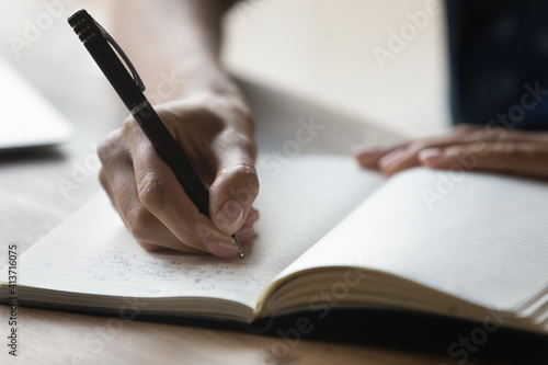 Close up African American woman writing in notebook, holding pen, businesswoman entrepreneur planning workday, meetings, managing time, student taking notes, preparing for exam, handwriting photo