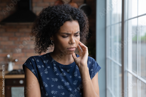 Close up upset thoughtful African American woman making difficult decision, thinking about personal problems, standing near window at home alone, lost in thoughts, worried about break up or divorce