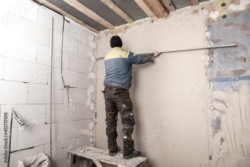 A worker plasters the walls in the room. © schankz