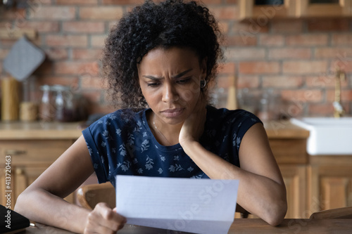 Close up unhappy African American young woman reading letter, document, frustrated businesswoman or student received bad news, unexpected debt or job dismissal notification, financial problem photo
