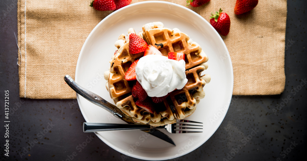 Overhead view of waffles garnished with strawberries and whipped cream Overhead view of waffles garnished with strawberries and whipped cream