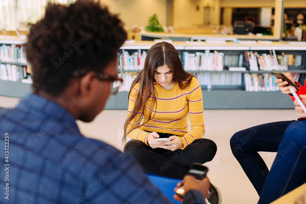 Friends using smart phones while sitting in library Friends using smart phones while sitting in library