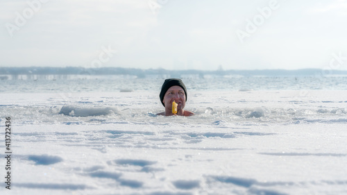 Man sitting in an ice hole while eating ice cream in winter © DZiegler