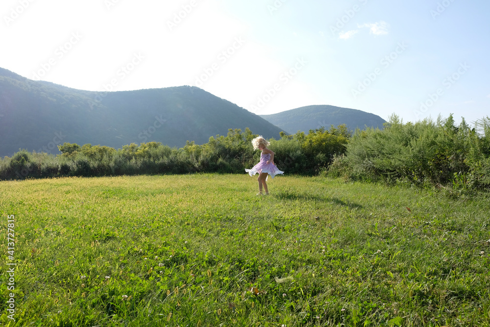 Playful girl spinning on grassy field against mountains and sky Playful girl spinning on grassy field against mountains and sky