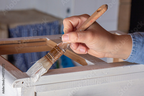 Close-up of a hand painting with a brush a furniture in white color