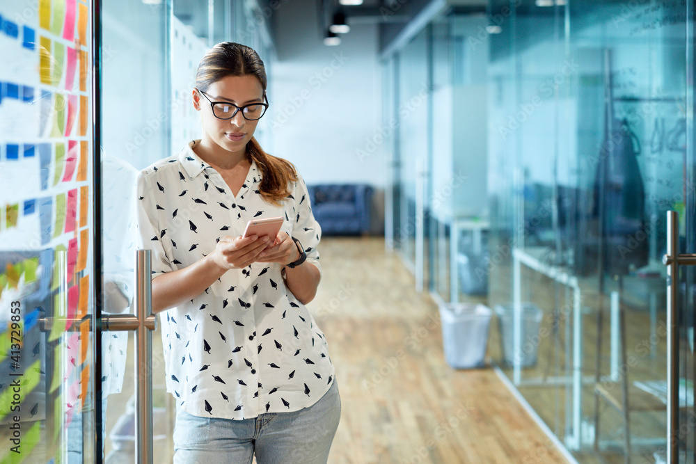 Businesswoman using mobile phone while leaning on glass door at corridor Businesswoman using mobile phone while leaning on glass door at corridor