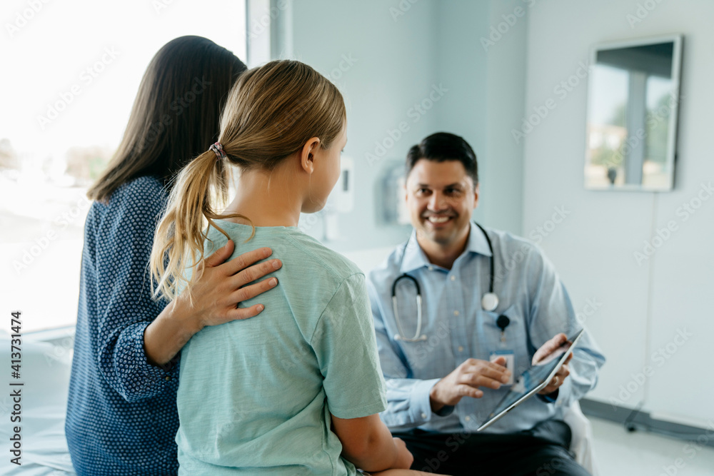 Cheerful pediatrician showing x-ray image on tablet computer to mother and daughter in medical examination room Cheerful pediatrician showing x-ray image on tablet computer to mother and daughter in medical examination room