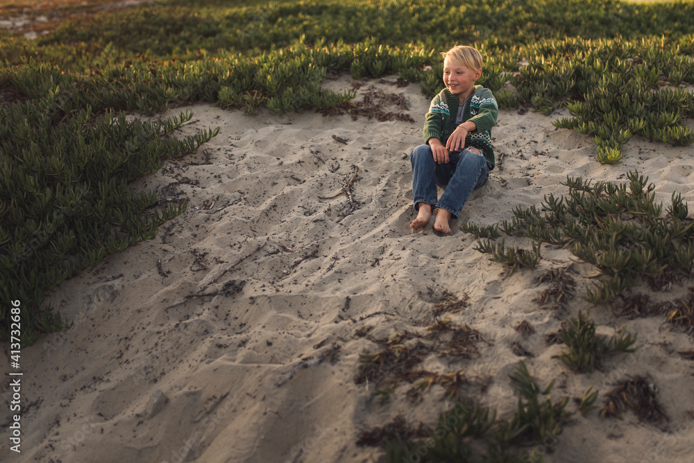 Full length of boy sitting on sand at beach during sunset Full length of boy sitting on sand at beach during sunset